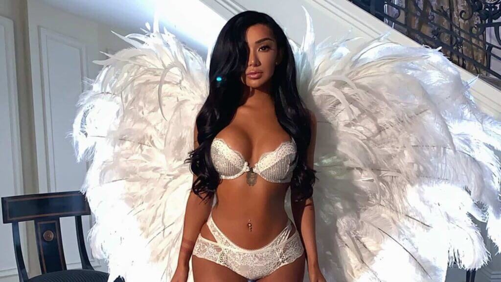 Woman wearing white lace lingerie and large white feathered angel wings standing indoors