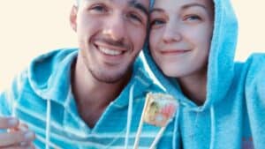 Smiling couple in blue hoodies holding sushi with chopsticks close to the camera