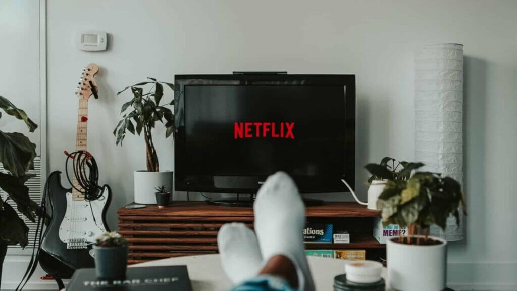 Person with white socks relaxing and watching Netflix on a Toshiba TV in a living room with guitar and plants