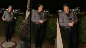 Female police officer in uniform and beanie talking to a person at night outside a house.
