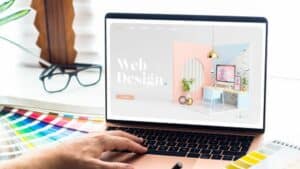 Person using a laptop displaying a web design page with color swatches and glasses on the desk.