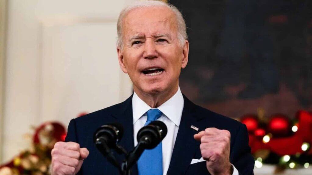 Joe Biden speaking passionately with clenched fists at a podium decorated for Christmas.
