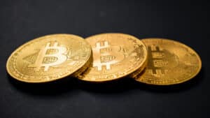 Three gold-colored physical Bitcoin coins on a dark surface.