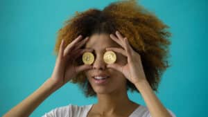 Woman holding two Bitcoin coins over her eyes against a blue background