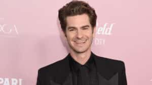 Andrew Garfield smiling in a black suit at a pink carpet event.