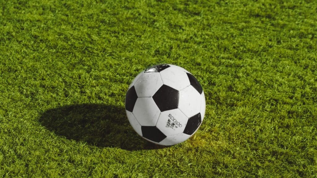 Black and white Adidas soccer ball on green grass field casting a shadow