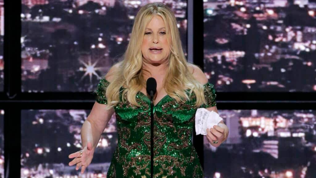 Blonde woman in a green sequined dress speaking at a microphone holding a crumpled paper on stage