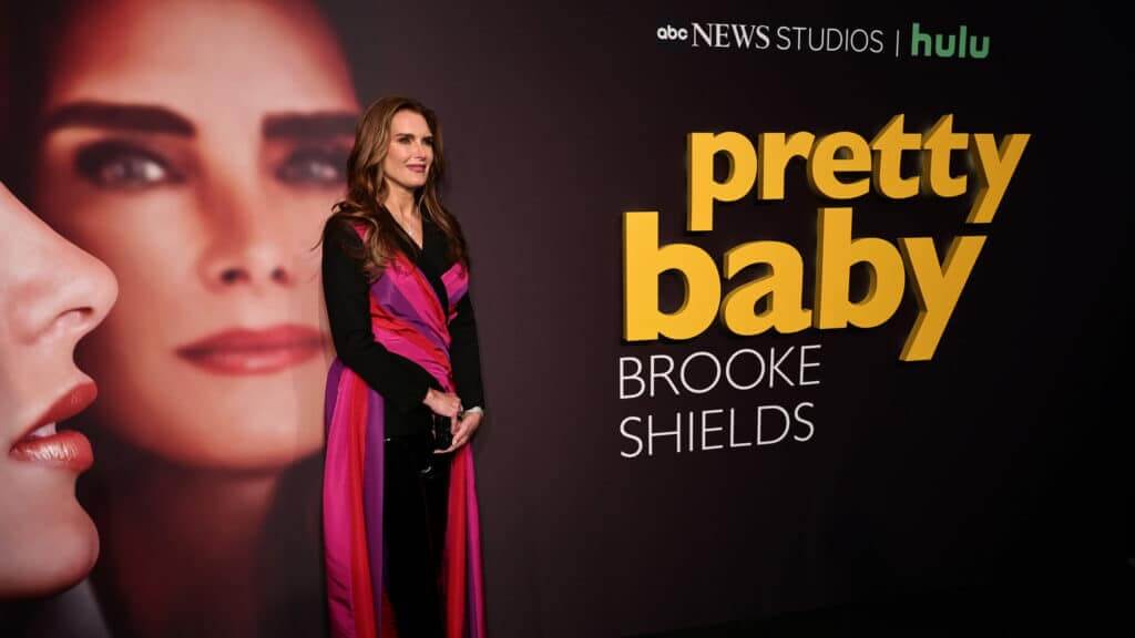 Brooke Shields standing in front of a Pretty Baby Hulu promotional backdrop at an event.