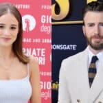 Young woman in white dress at event and man in white suit with striped tie at premiere backdrop