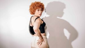 Ice Spice poses and looks over her shoulder in front of a white wall.
