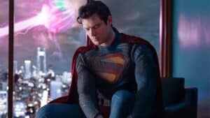 Superman in his suit sitting with eyes closed against a cityscape at night with a glowing pink energy orb outside the window.