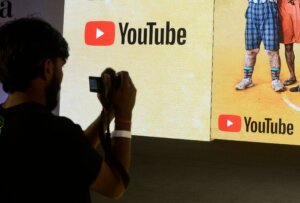 Person taking a photo of a screen displaying the YouTube logo and part of two people wearing shorts and sneakers