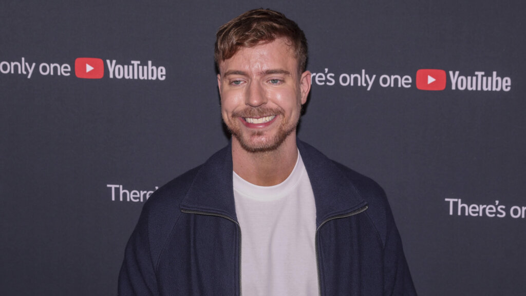 Smiling man with light brown hair and beard wearing a navy jacket and white shirt at a YouTube event backdrop