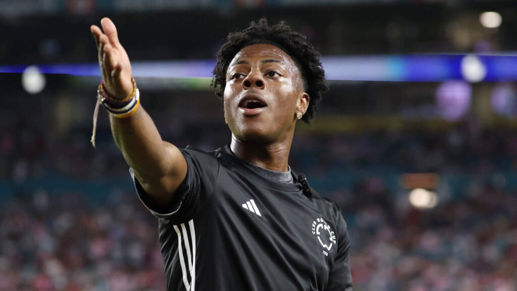 Soccer player in black Adidas Club World Cup jersey gesturing and speaking on the field