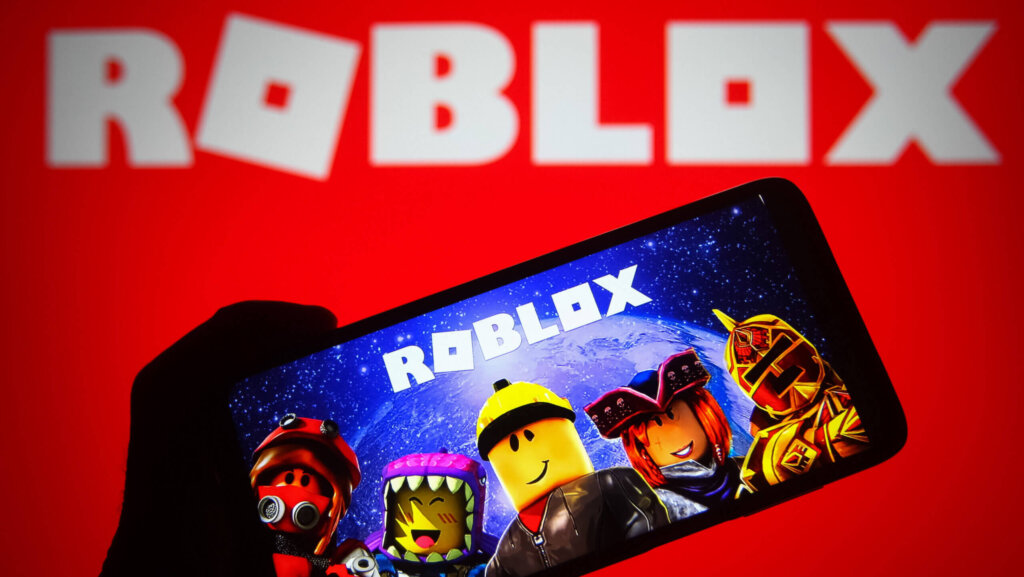 Hand holding smartphone displaying Roblox game characters with Roblox logo on red background