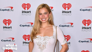 Blonde woman smiling in white lace dress at iHeartRadio event with Capital One logos in background