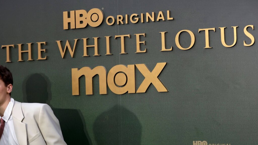 HBO Original The White Lotus Max logo on a dark green backdrop with a person in a beige suit partially visible on the left