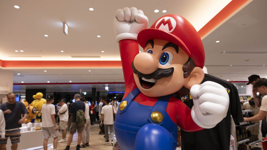 Large statue of Nintendo's Mario character with raised fist in a busy indoor event space.