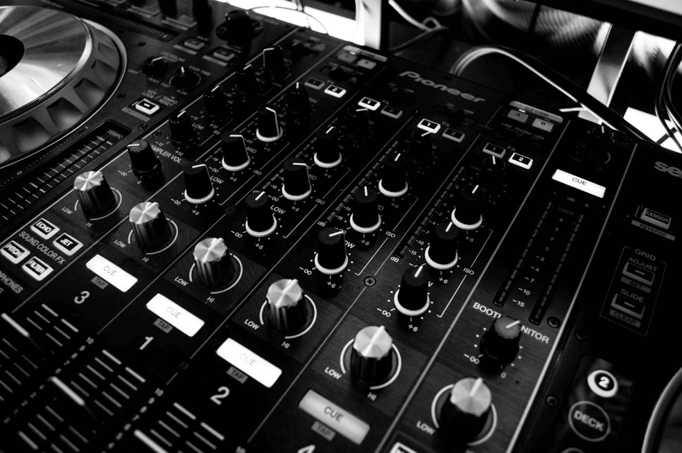 Pioneer DJ mixer with multiple knobs, sliders, and cue buttons in black and white.
