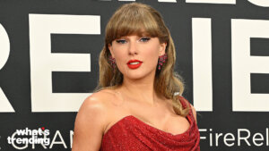 Taylor Swift wearing a red dress and matching earrings at a formal event with a black and white backdrop.