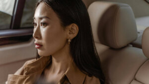 Woman with long dark hair and gold hoop earrings sitting in a car seat looking out the window.