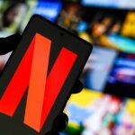 Hand holding smartphone displaying the Netflix logo with a blurred streaming content background