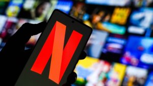 Hand holding smartphone displaying the Netflix logo with a blurred streaming content background