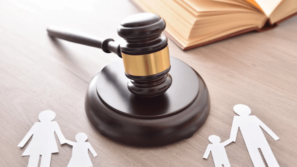 Wooden judge gavel with paper cutouts of a family and an open book on a table.