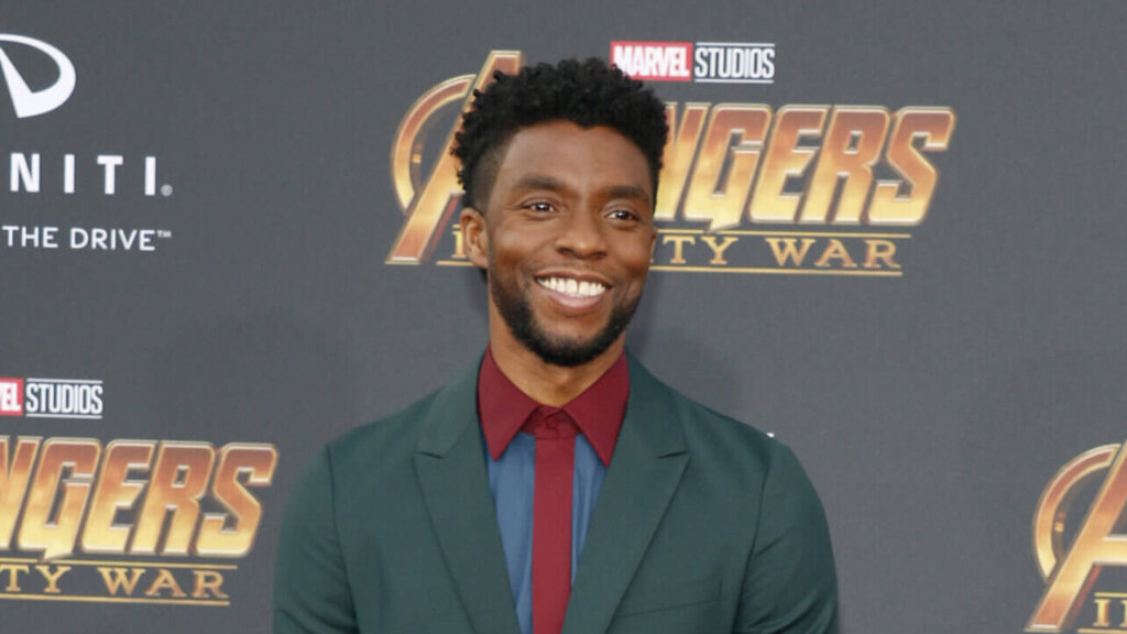 Chadwick Boseman smiling in a green suit at the Avengers Infinity War premiere on a purple carpet.