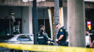 Three police officers standing behind yellow caution tape in an urban area.