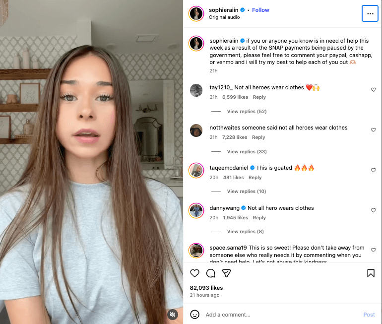 Young woman with long brown hair wearing a gray shirt speaking in a home setting with patterned wallpaper and shelves behind her
