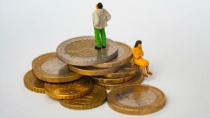 Miniature man standing and woman sitting on stacked Euro coins representing financial disparity